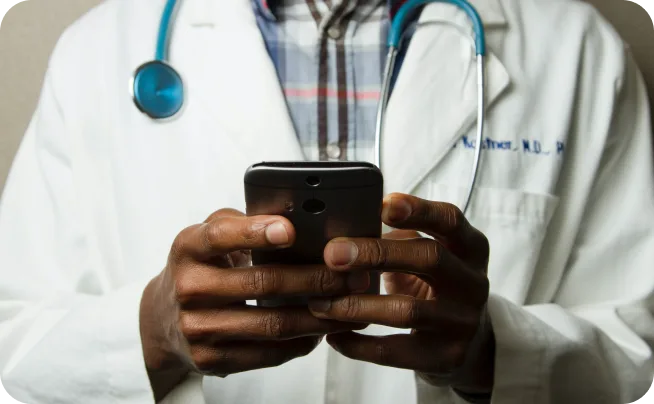 Clinician in a white coat with a stethoscope looking at a smartphone held in both hands