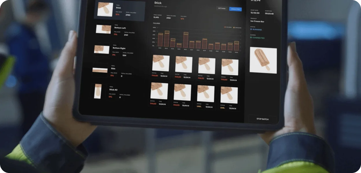 Hands holding a tablet running a machine-vision inspection dashboard with defect fail rates and failed frames from ice cream production