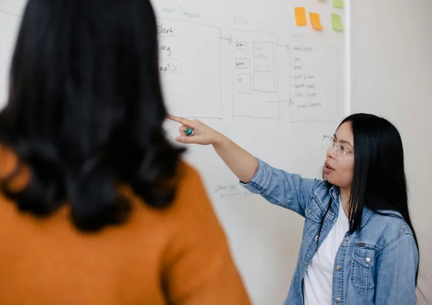 Two team members working through notes on a whiteboard