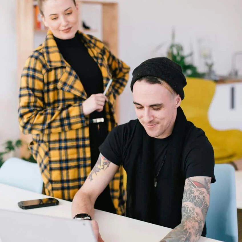 A colleague standing beside a seated developer working on a laptop