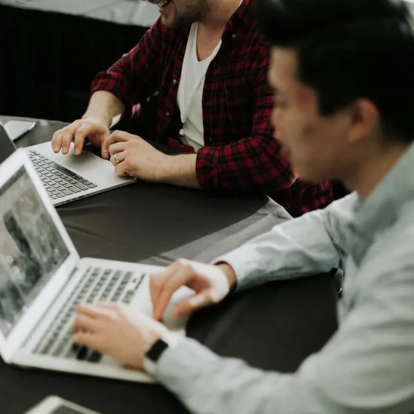 Two people working on laptops across a dark table