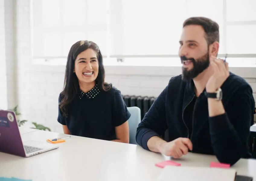 Two colleagues smiling during a meeting at a white table