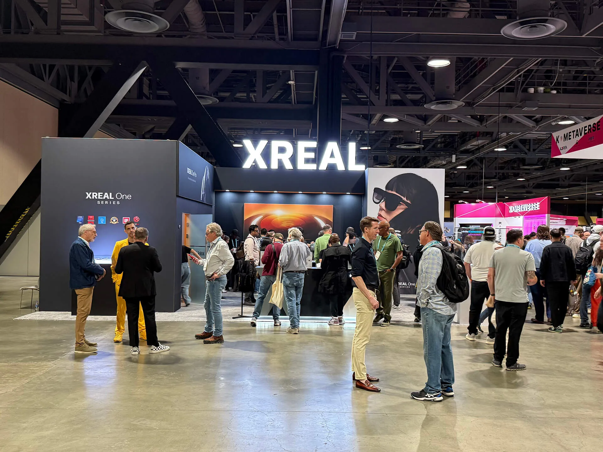 Trade-show crowd in front of a large illuminated XREAL booth showing the XREAL One series