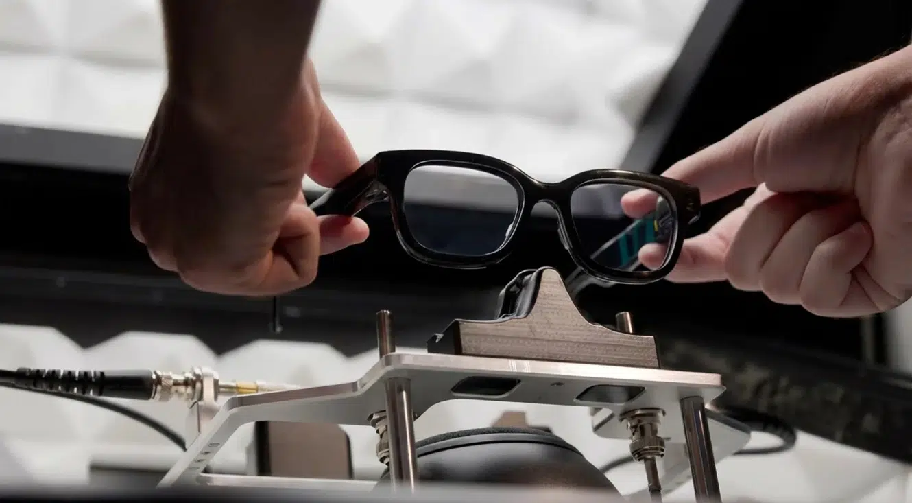 Hands positioning a pair of AR smart glasses onto a hardware testing rig inside a lab environment.