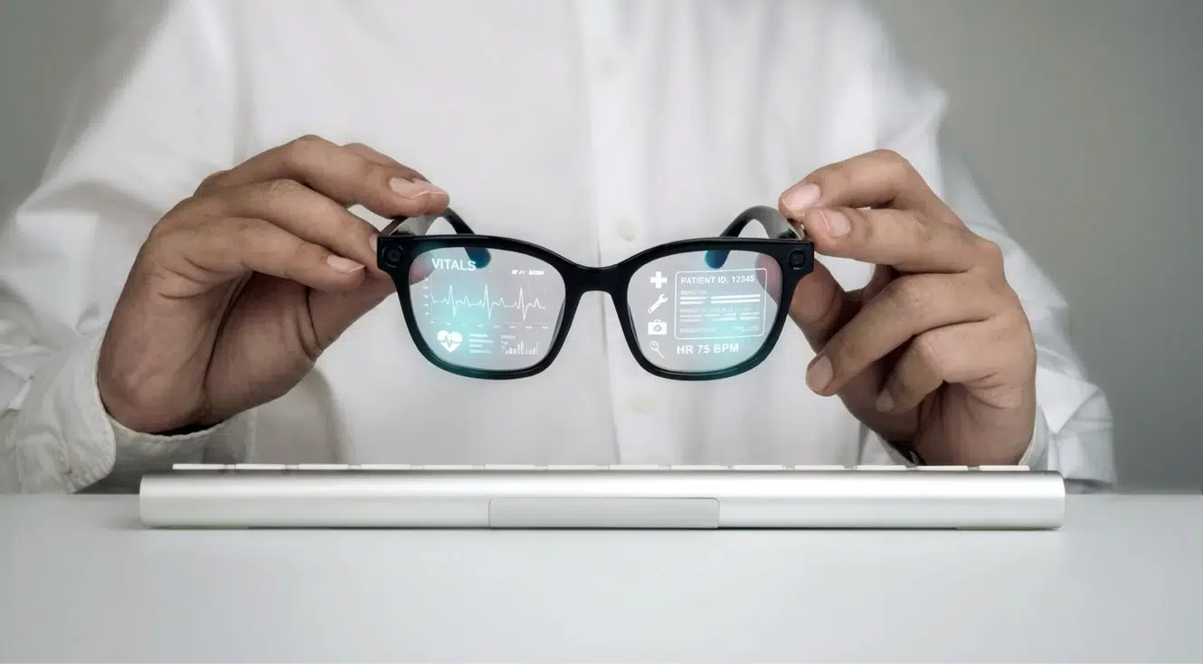 Person holding AR smart glasses that display patient vitals and medical information on the lenses.