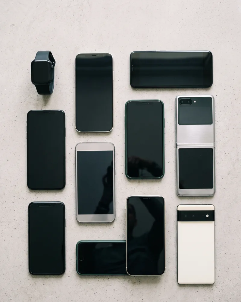 Eight smartphones of different sizes and finishes laid out with a smartwatch