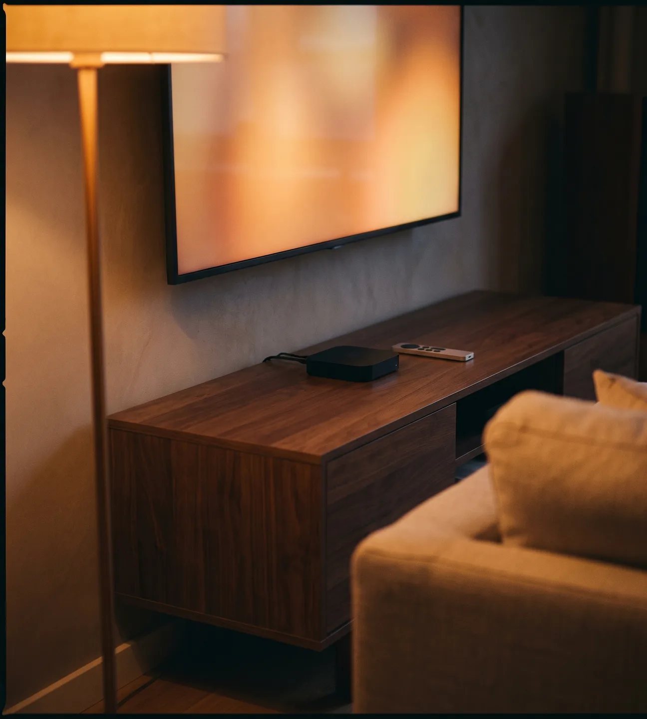 Living-room television and streaming box on a walnut console in warm evening light