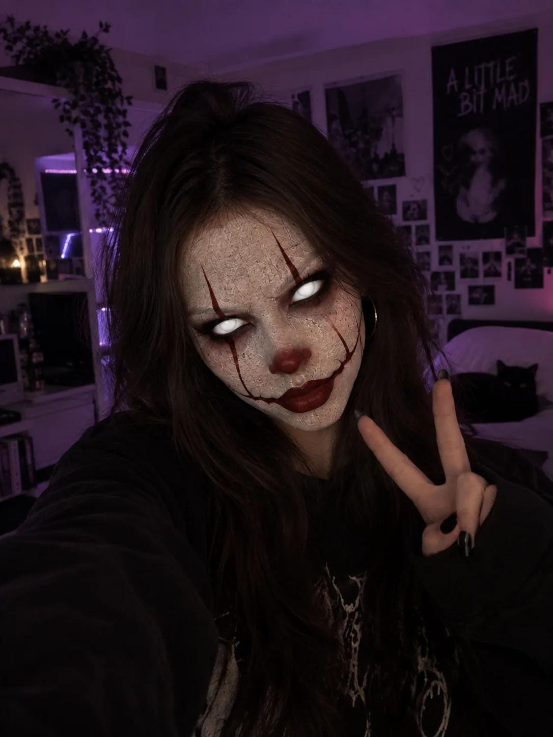 Fan in a purple-lit room flashing a peace sign while wearing a white-faced clown mask