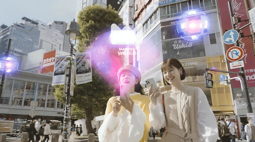 Two young women on a Tokyo street laughing at a glowing AR character and floating orbs
